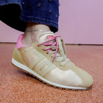 Beige sneaker with pink laces worn by a person on a pink floor.