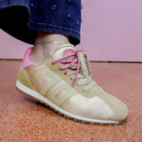 Beige sneaker with pink laces worn by a person on a pink floor.