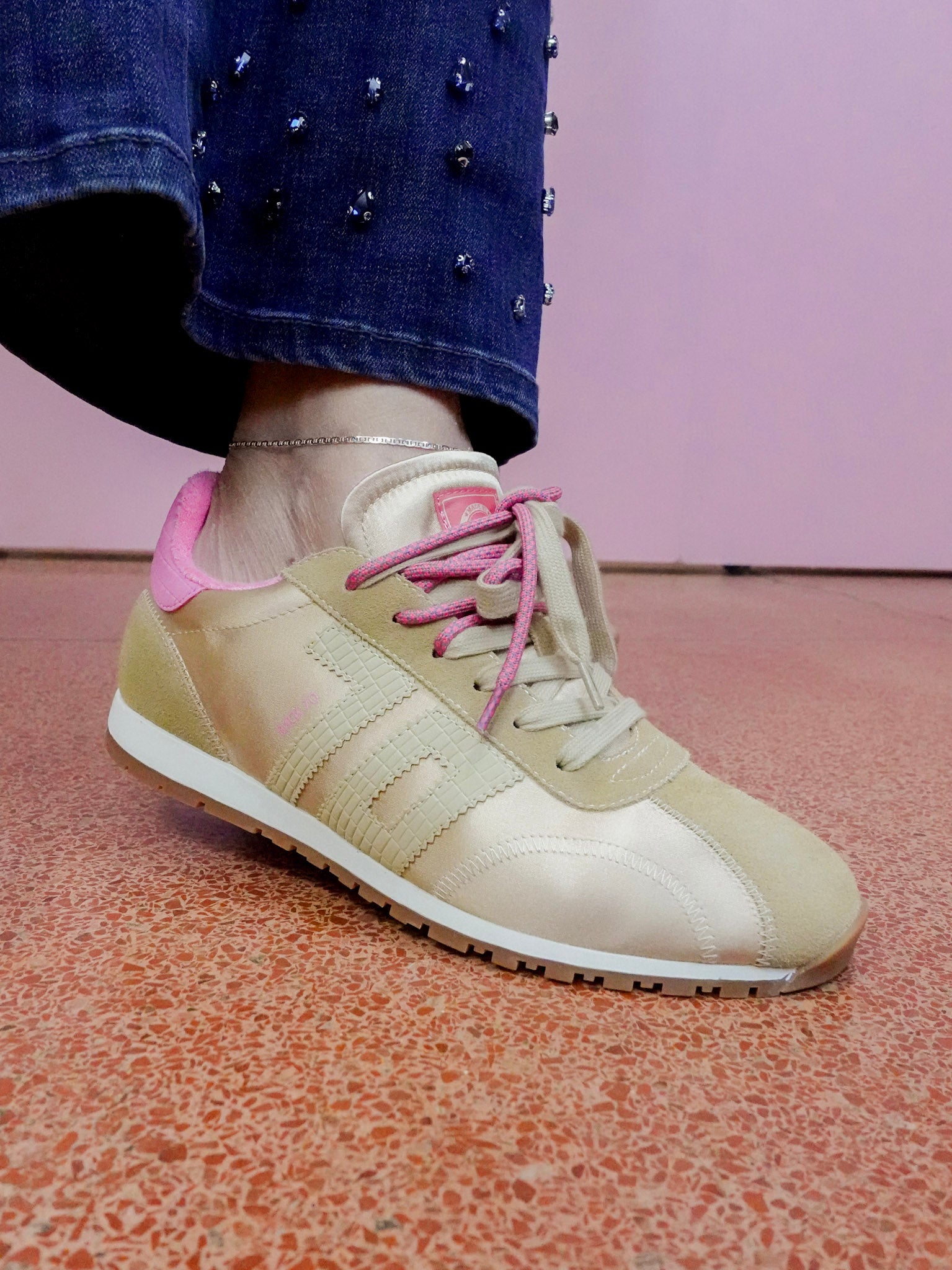 Beige sneaker with pink laces worn by a person on a pink floor.