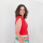 Woman wearing a red top and colorful floral skirt against a white background