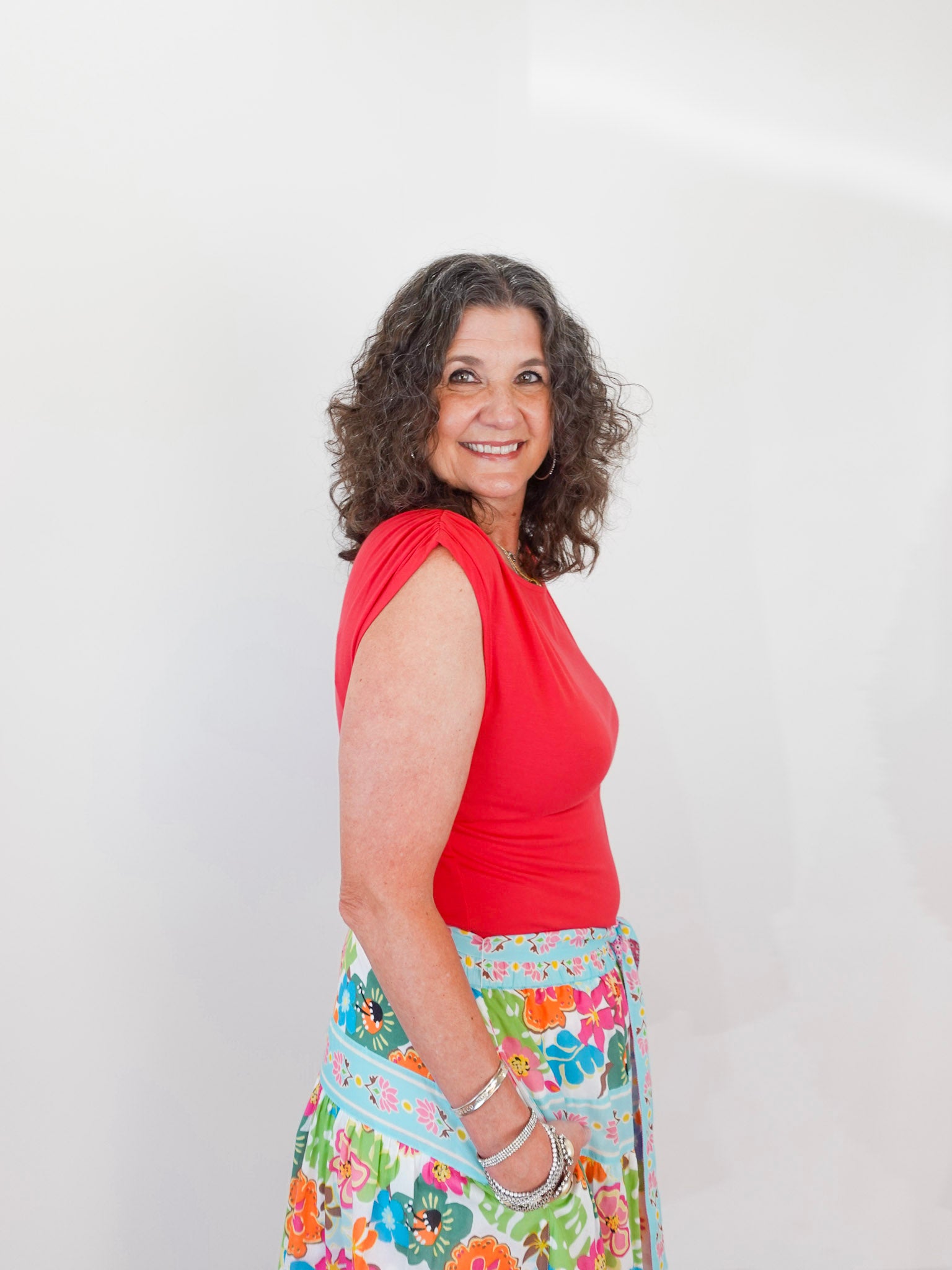 Woman wearing a red top and colorful floral skirt against a white background
