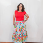 Woman wearing a red top and colorful floral skirt against a white background