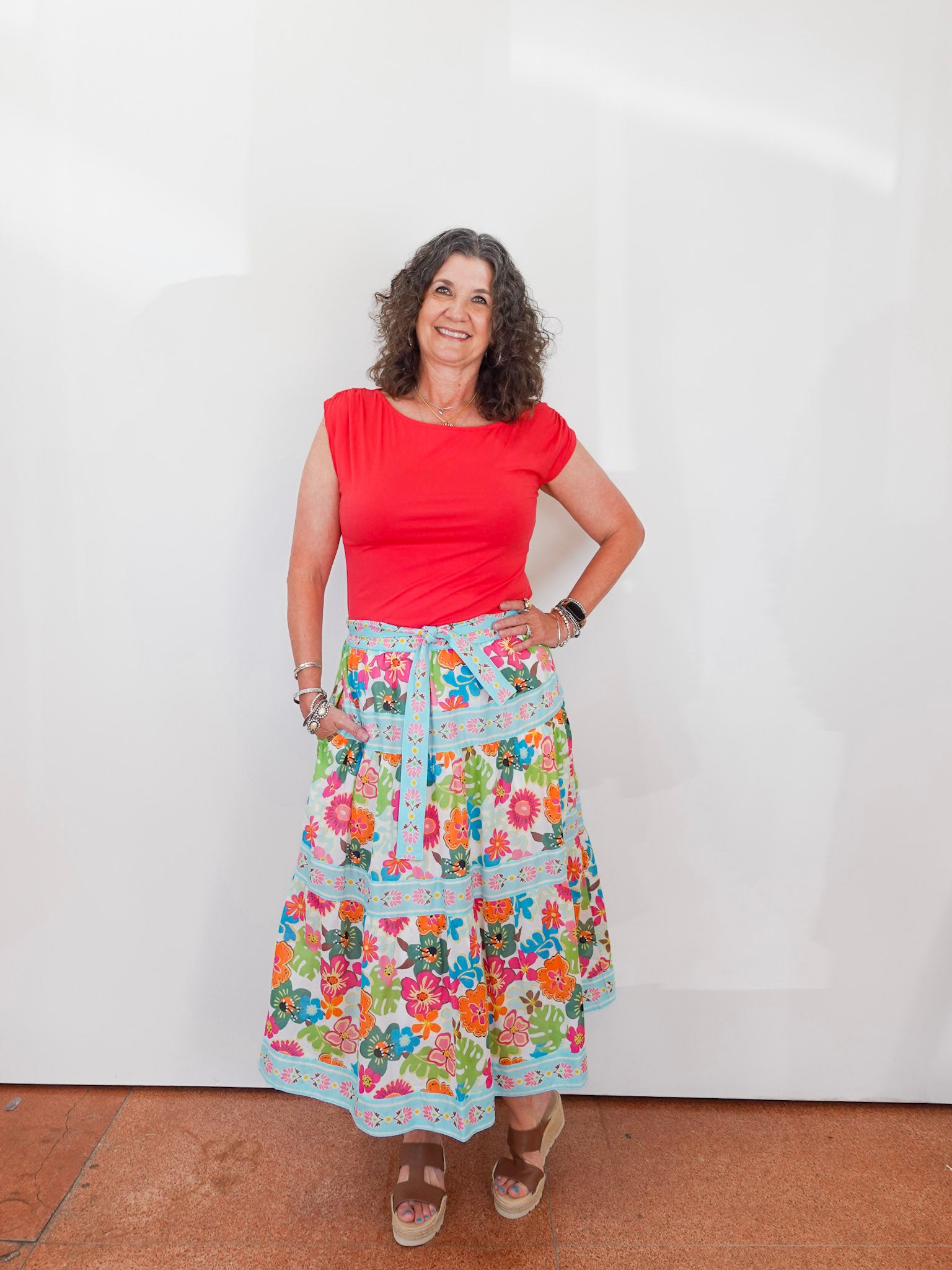 Woman wearing a red top and colorful floral skirt against a white background