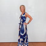 Woman wearing a blue patterned dress against a white wall.
