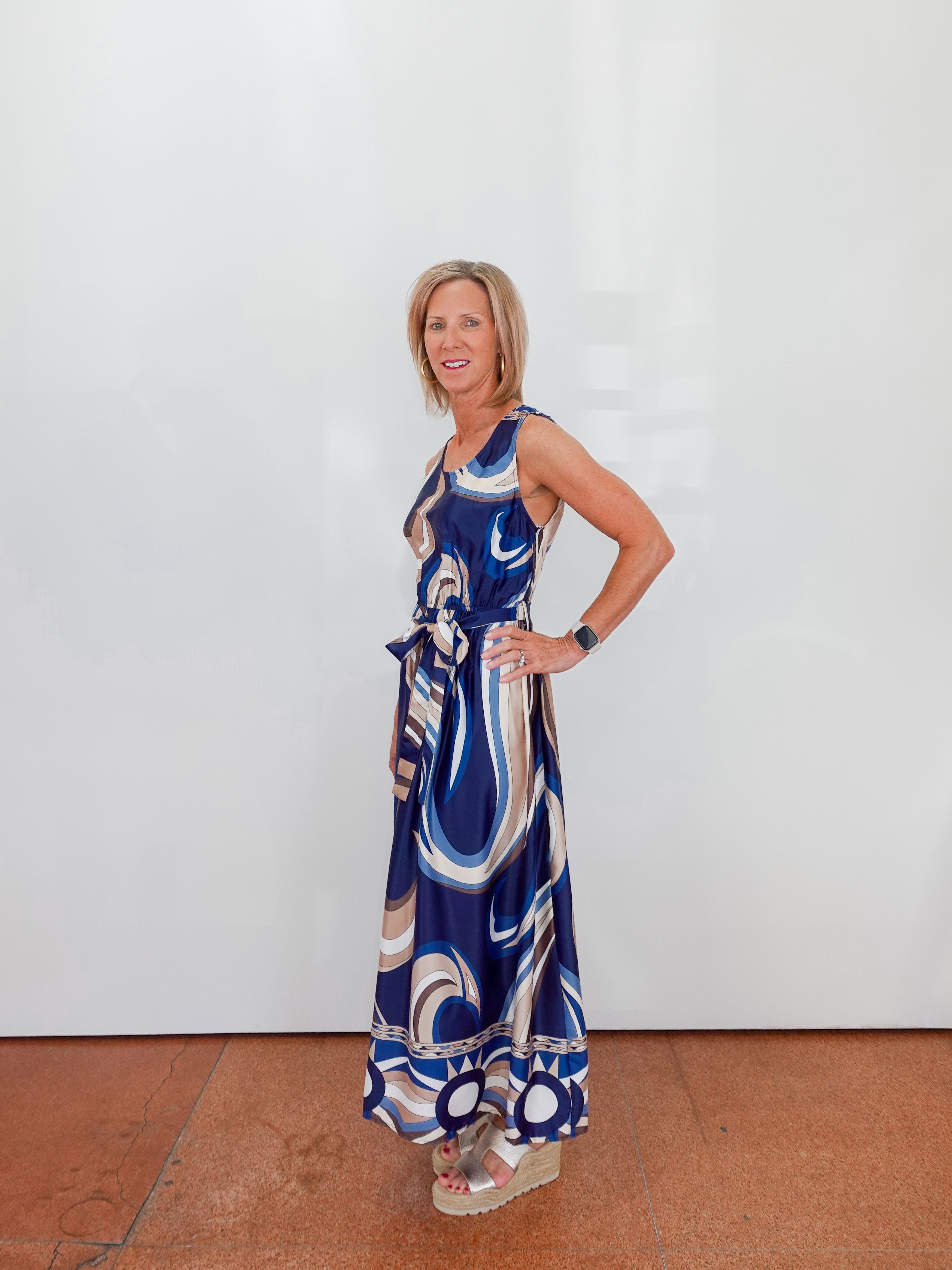 Woman wearing a blue patterned dress against a white wall.