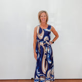 Woman wearing a blue patterned dress against a white wall.