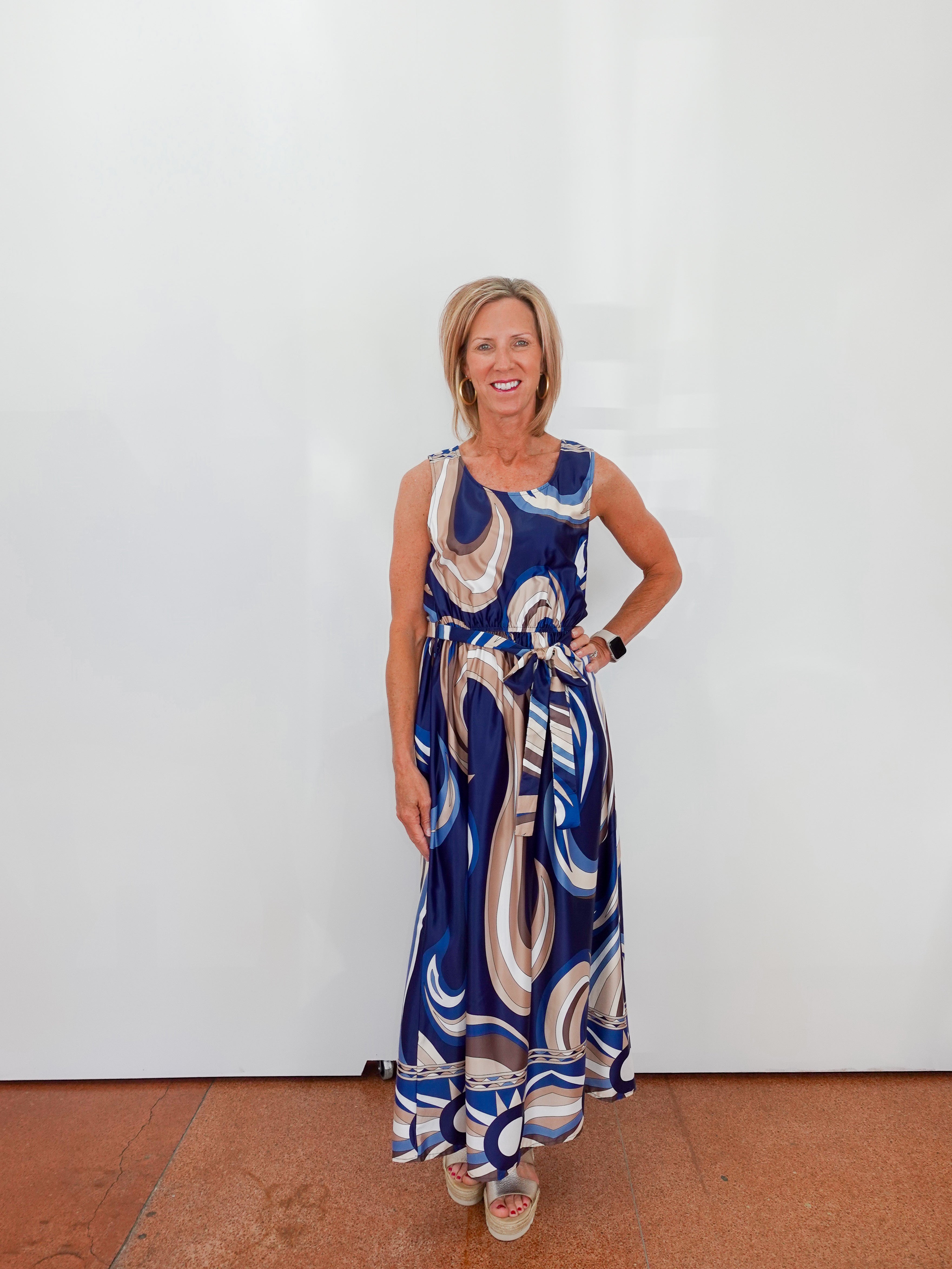 Woman wearing a blue patterned dress against a white wall.