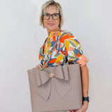 Woman holding a large beige tote bag with a bow detail against a plain background
