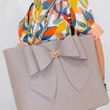 Gray handbag with a large bow held by a person wearing a colorful floral dress.