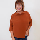 Woman wearing a brown top and glasses against a white background