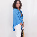 Woman wearing a blue shawl and white pants against a white background