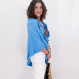 Woman wearing a blue shawl and white pants against a white background