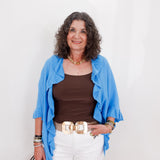 Woman wearing a blue cardigan, brown top, white pants, and carrying a handbag against a white background