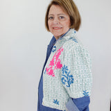 Woman wearing a colorful jacket with floral patterns against a white wall.