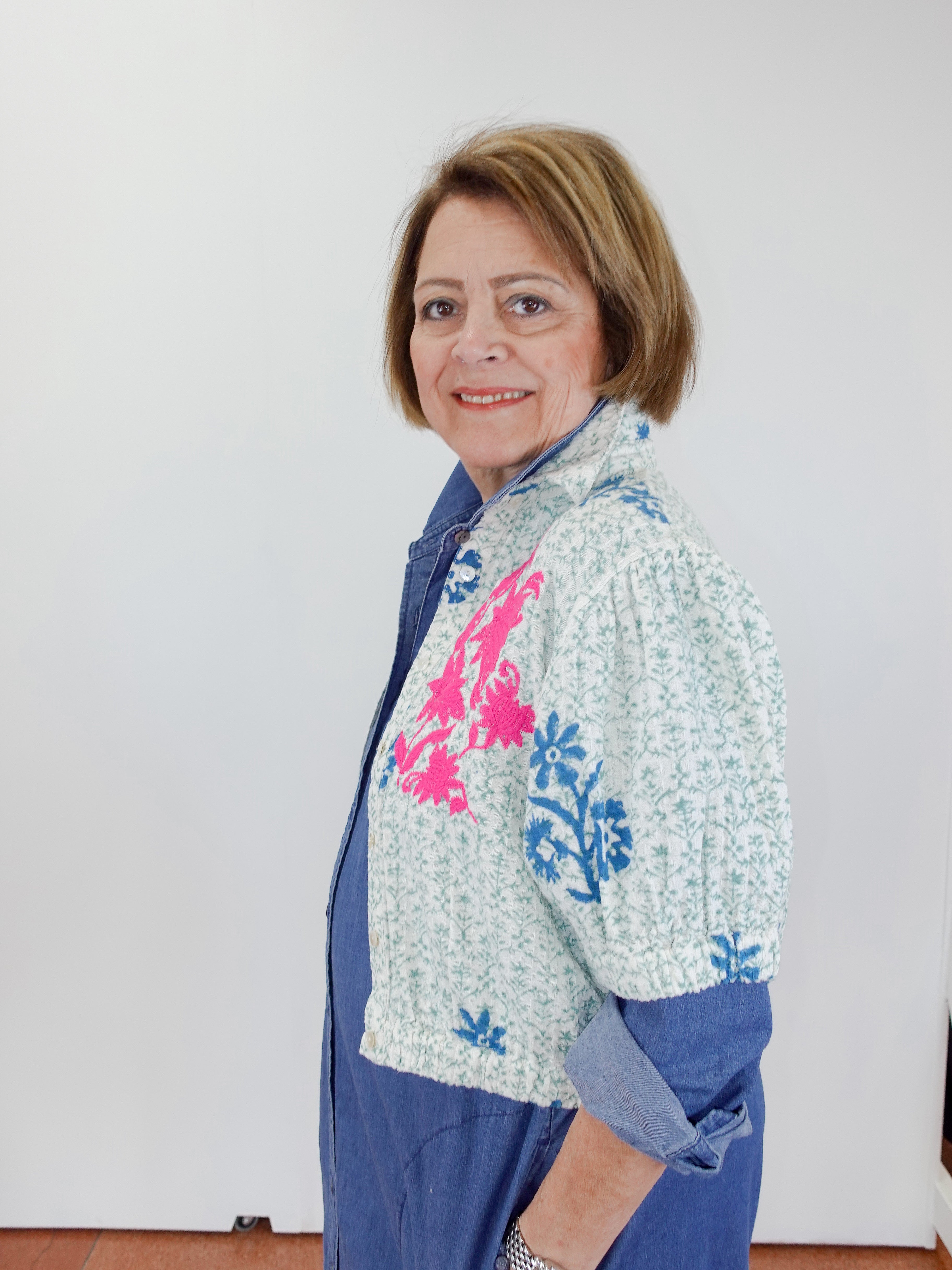Woman wearing a colorful jacket with floral patterns against a white wall.