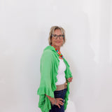 Woman wearing a green shawl over a white top and blue jeans against a white background