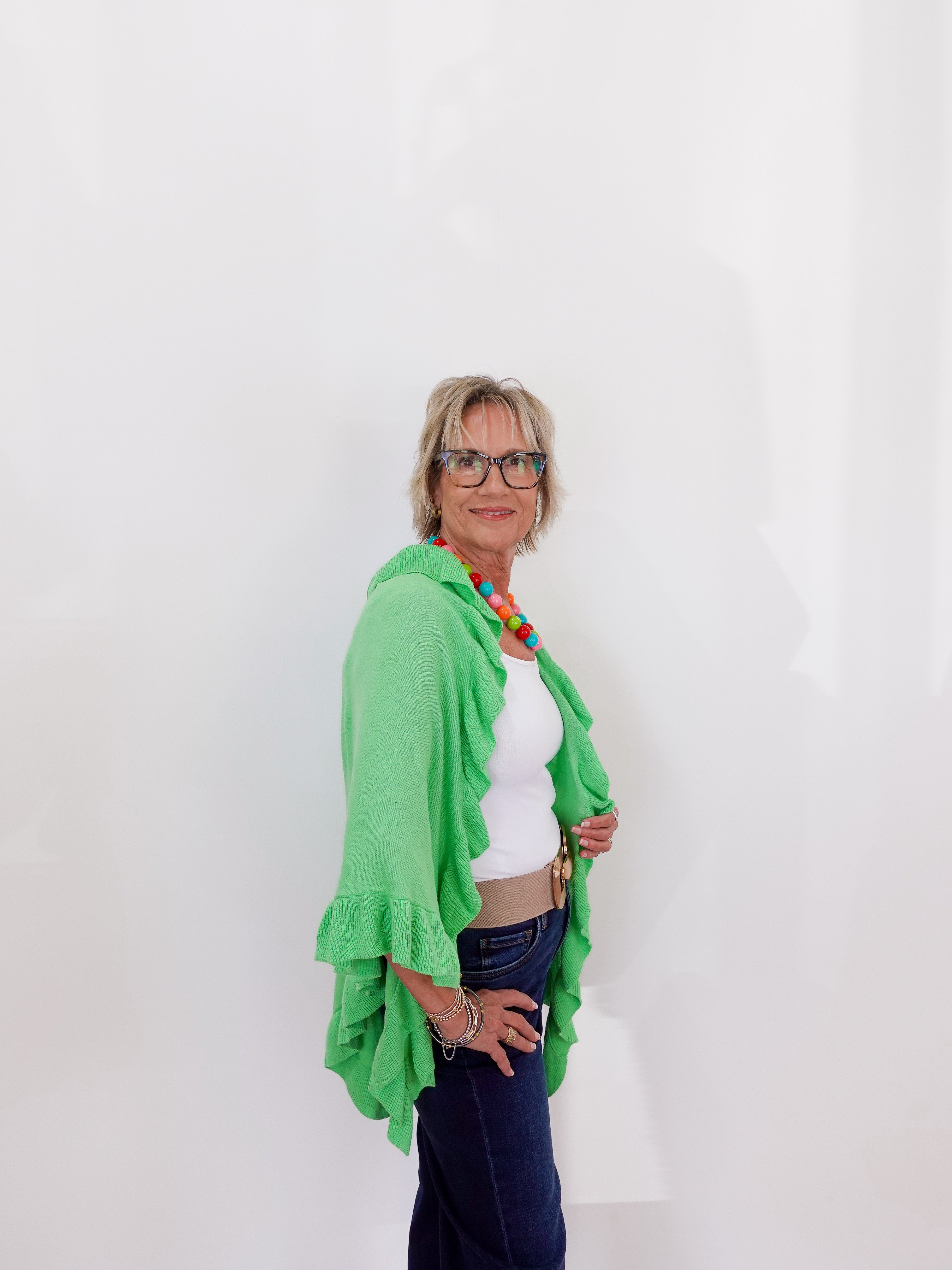 Woman wearing a green shawl over a white top and blue jeans against a white background