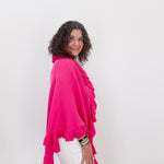 Woman wearing a bright pink top and white pants against a plain background