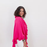 Woman wearing a bright pink top and white pants against a plain background