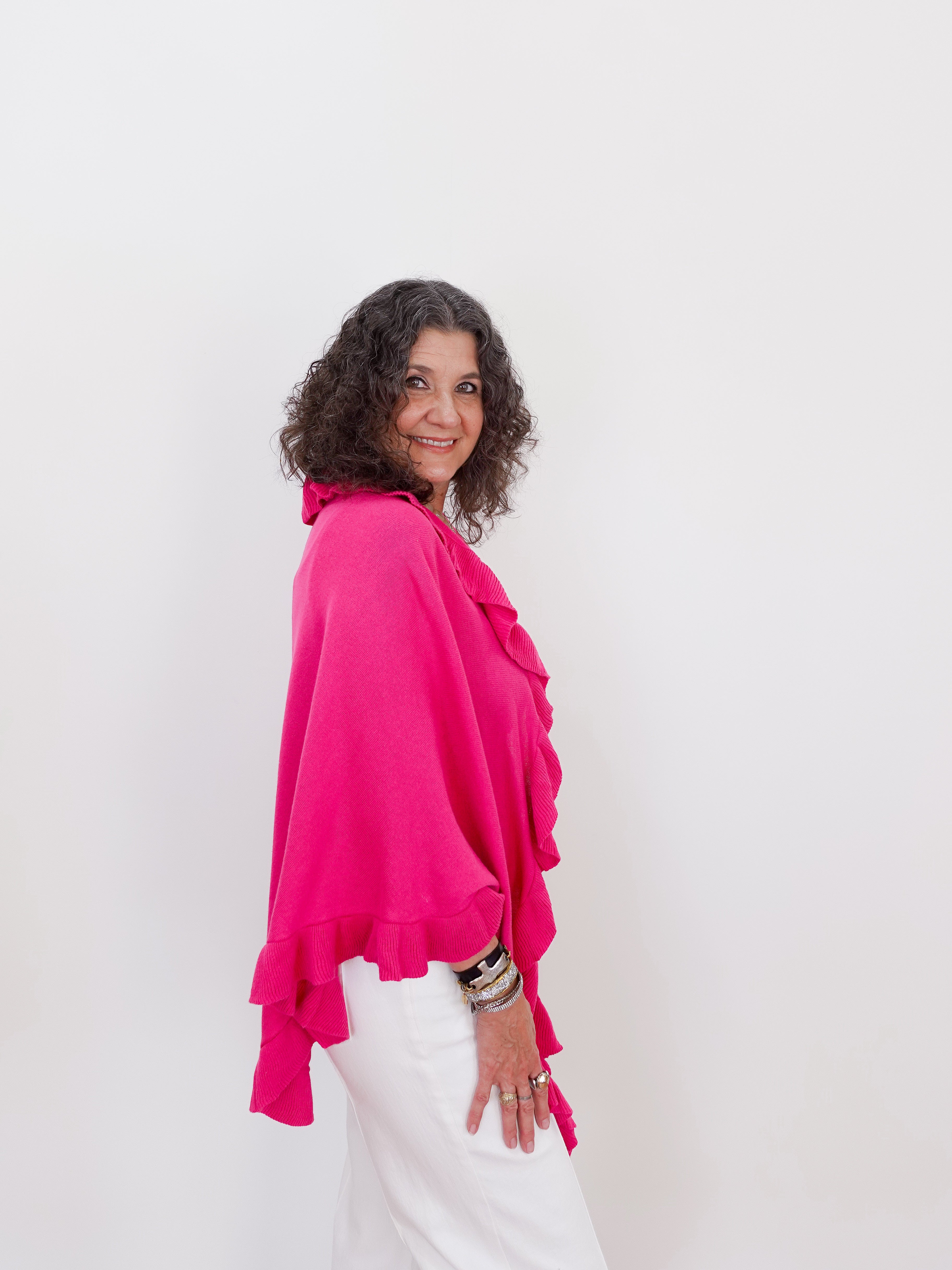 Woman wearing a bright pink top and white pants against a plain background