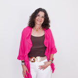 Woman wearing a pink cardigan, brown top, and white pants on a white background