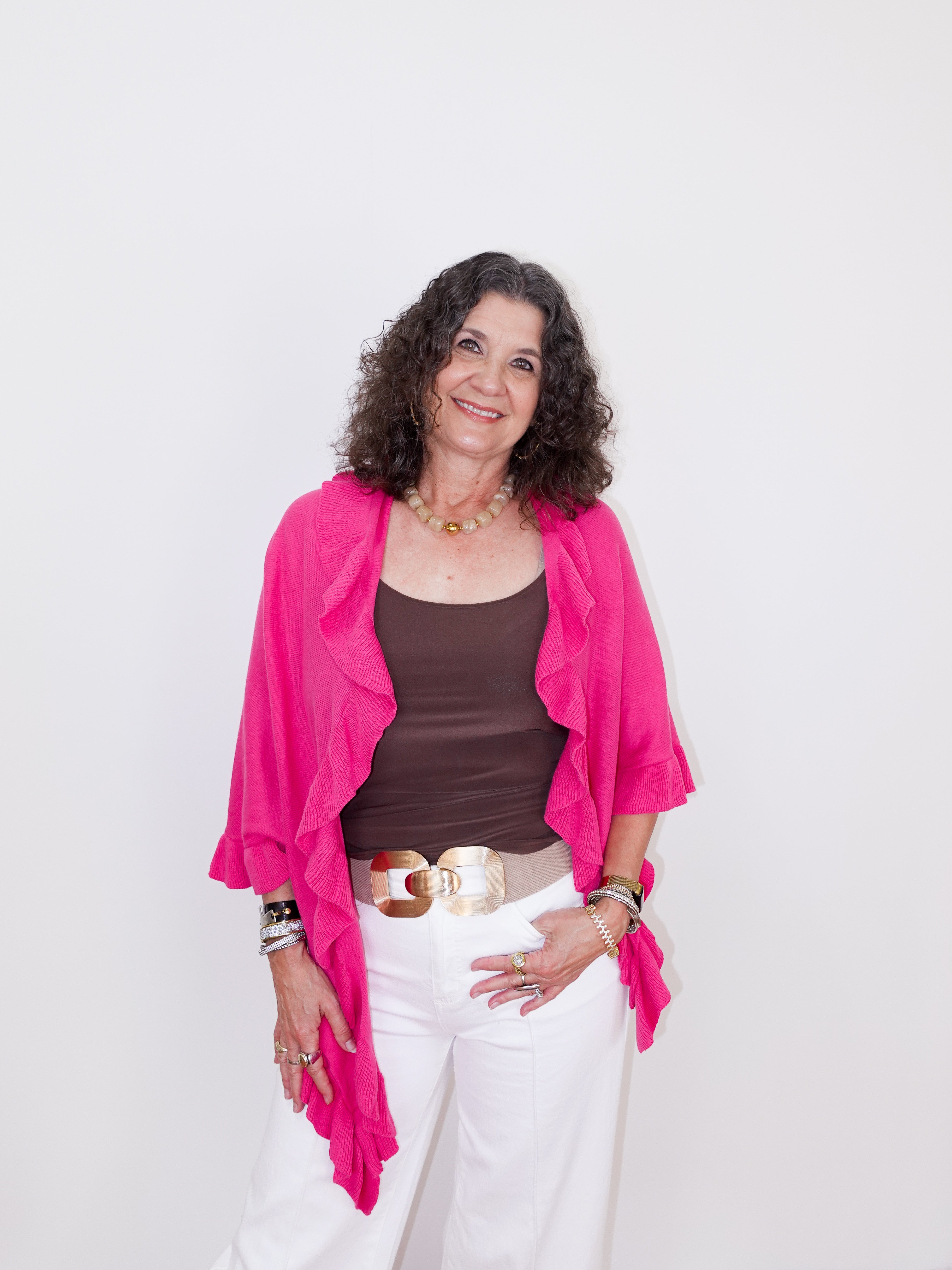 Woman wearing a pink cardigan, brown top, and white pants on a white background