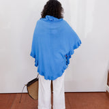 Person wearing a blue poncho and white pants against a white wall.