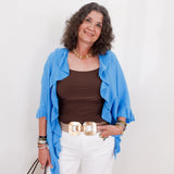 Woman wearing a blue jacket, brown top, and white pants against a white background