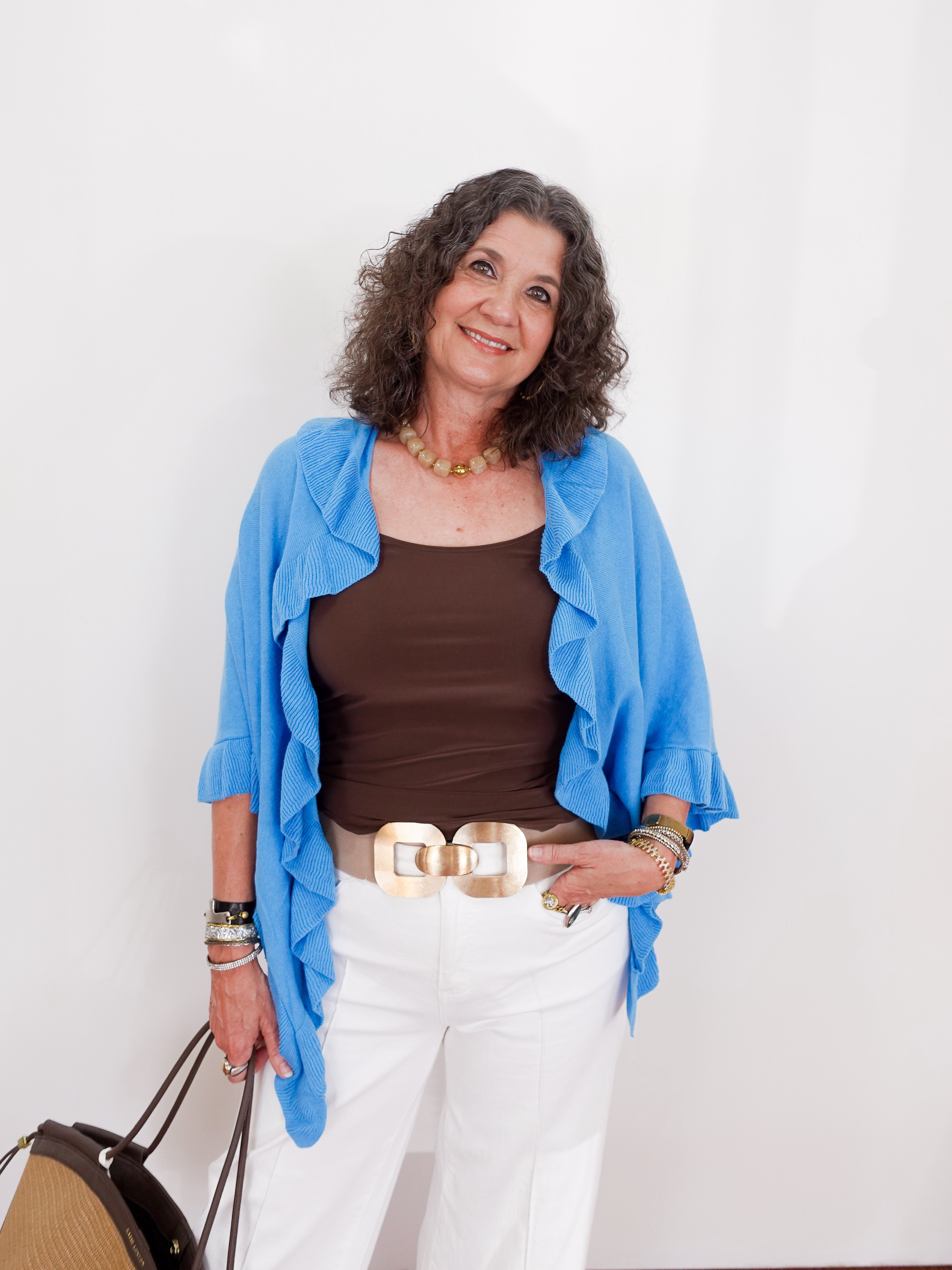 Woman wearing a blue jacket, brown top, and white pants against a white background