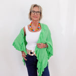 Woman wearing a green cardigan, white top, and blue jeans against a white background