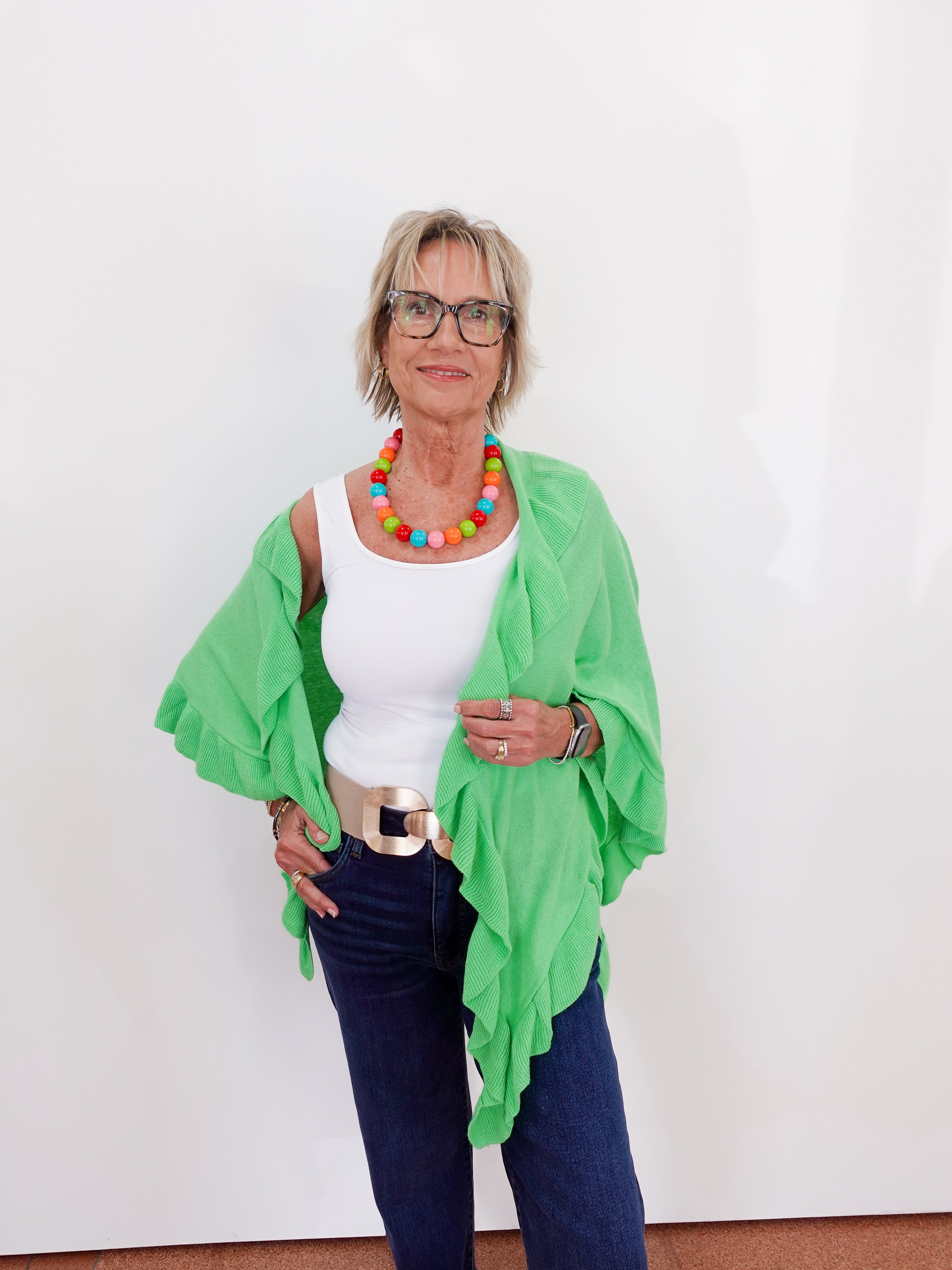 Woman wearing a green cardigan, white top, and blue jeans against a white background