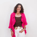 Woman wearing a bright pink cardigan over a brown top and white pants on a light gray background