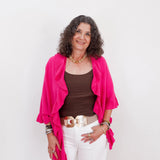 Woman wearing a bright pink cardigan over a brown top and white pants on a light gray background