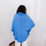 Person wearing a blue shawl against a white wall