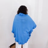 Person wearing a blue shawl against a white wall