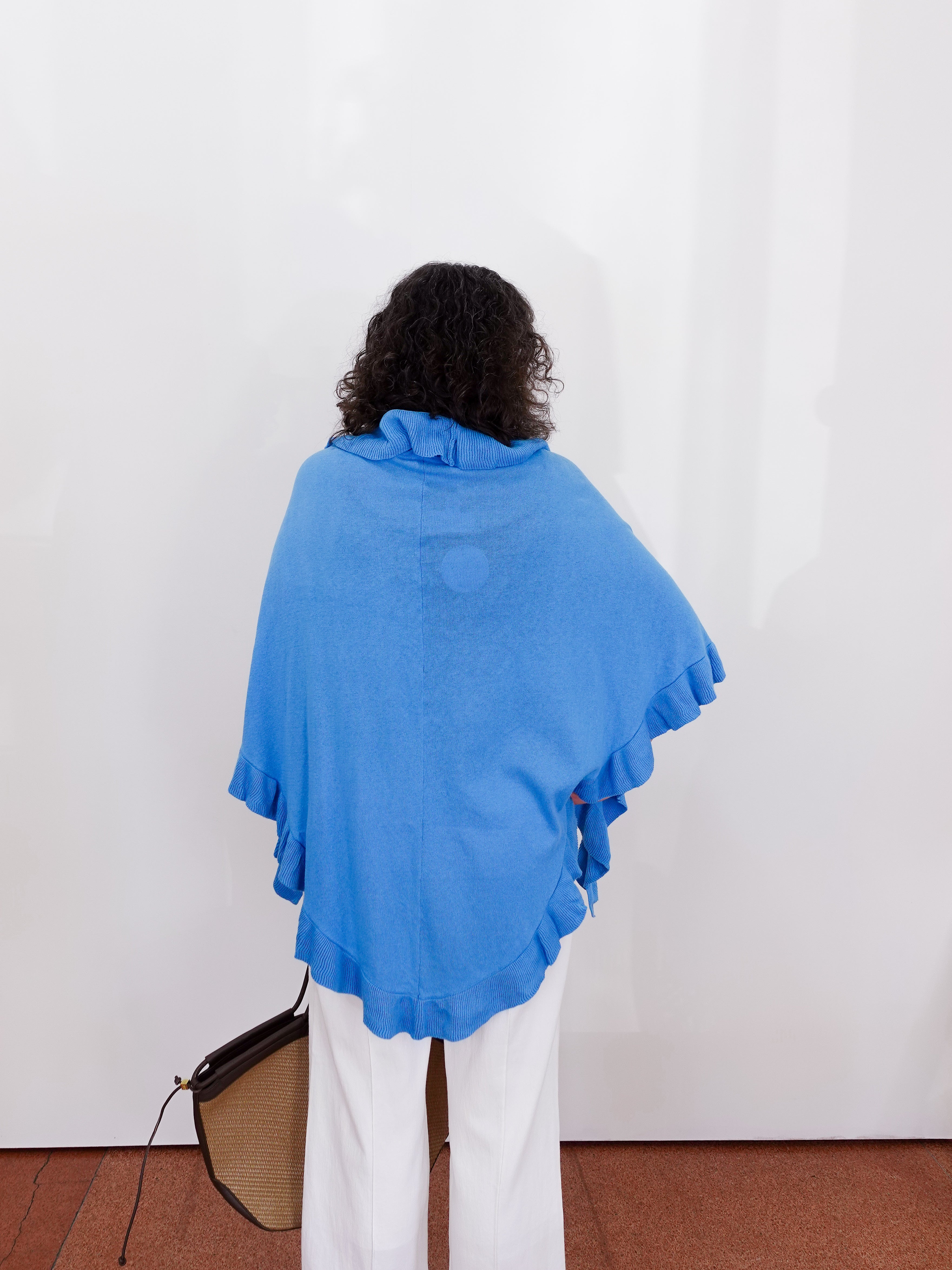 Person wearing a blue shawl against a white wall