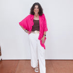 Woman wearing a bright pink top, white pants, and sandals on a plain background