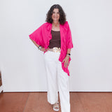 Woman wearing a bright pink top, white pants, and sandals on a plain background
