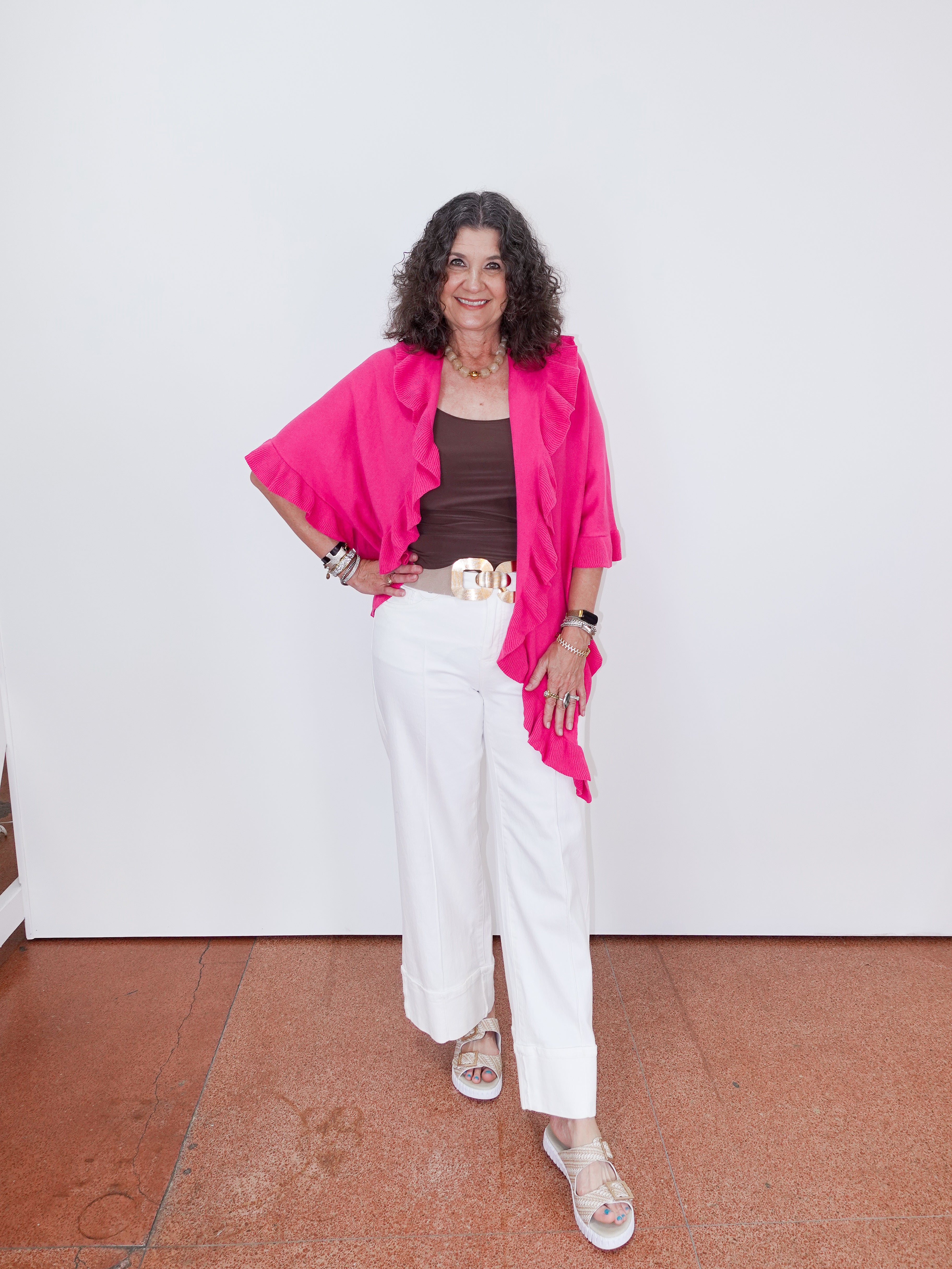 Woman wearing a bright pink top, white pants, and sandals on a plain background