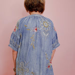 Person wearing a blue embroidered dress against a pink background