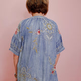 Person wearing a blue embroidered dress against a pink background