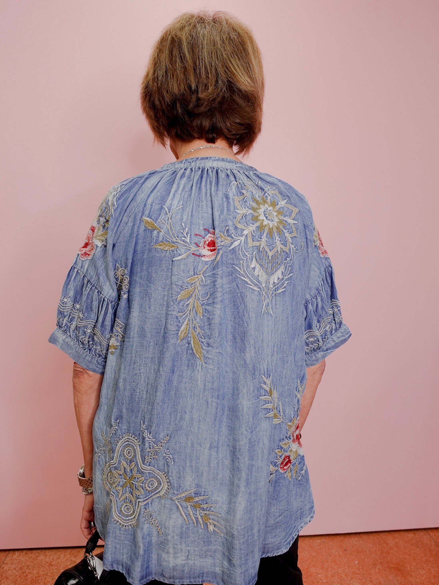 Person wearing a blue embroidered dress against a pink background