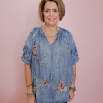 Woman wearing a blue embroidered blouse against a pink background