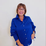 Woman wearing a blue shirt and white pants against a plain background