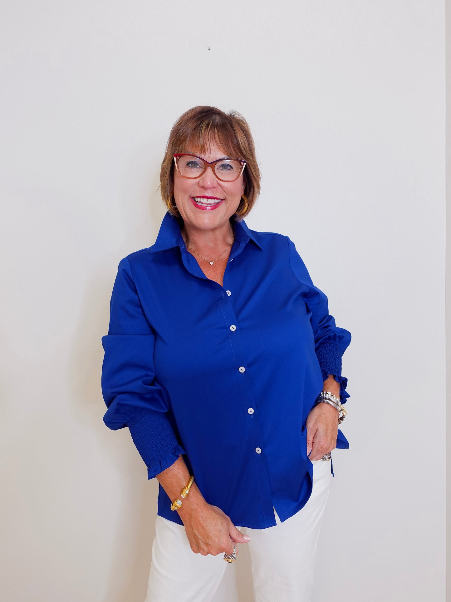 Woman wearing a blue shirt and white pants against a plain background