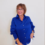 Woman wearing a blue shirt and white pants against a plain background