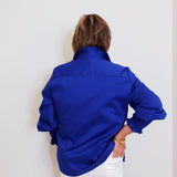 Person wearing a blue shirt and white pants against a plain background
