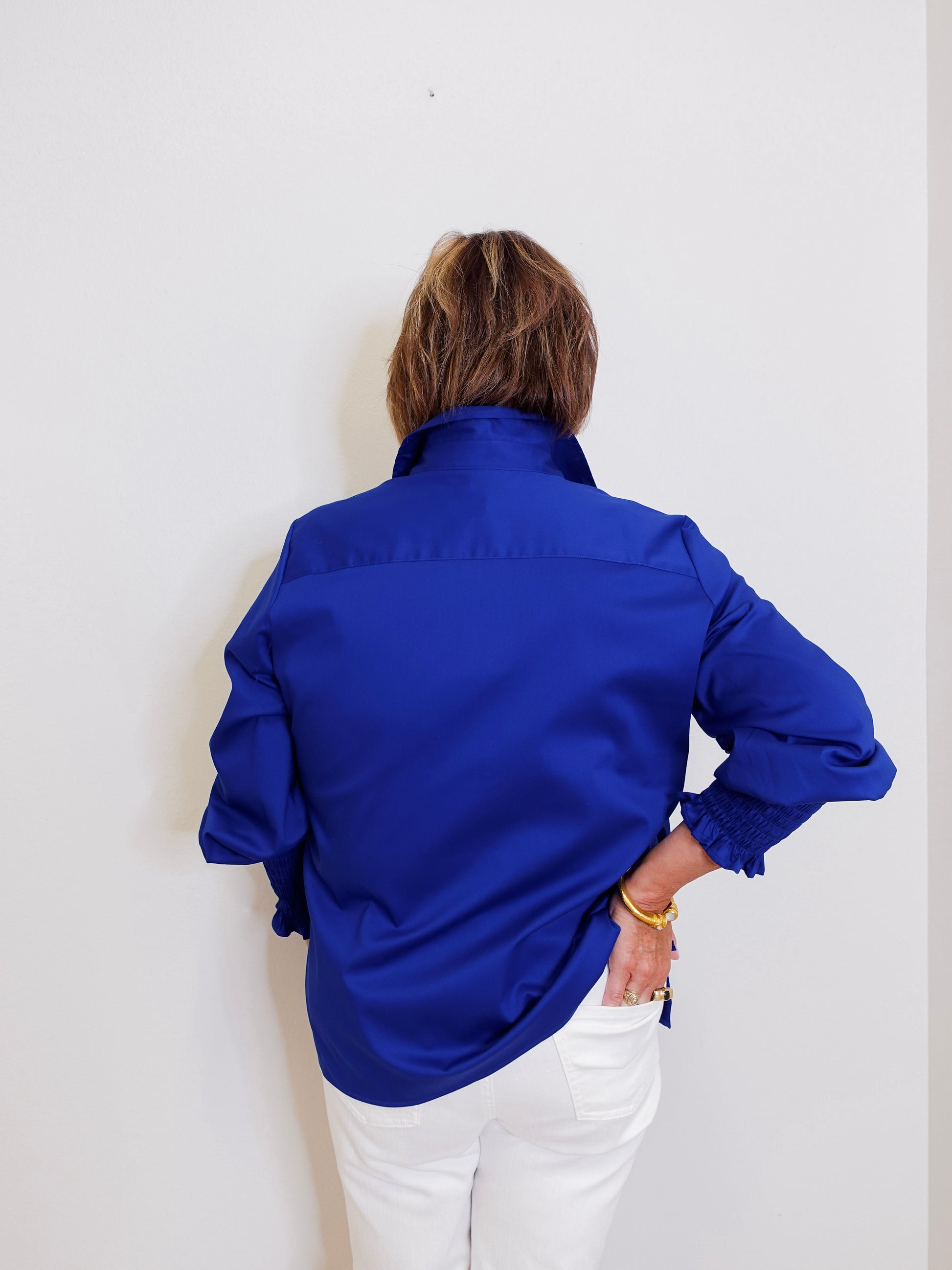 Person wearing a blue shirt and white pants against a plain background