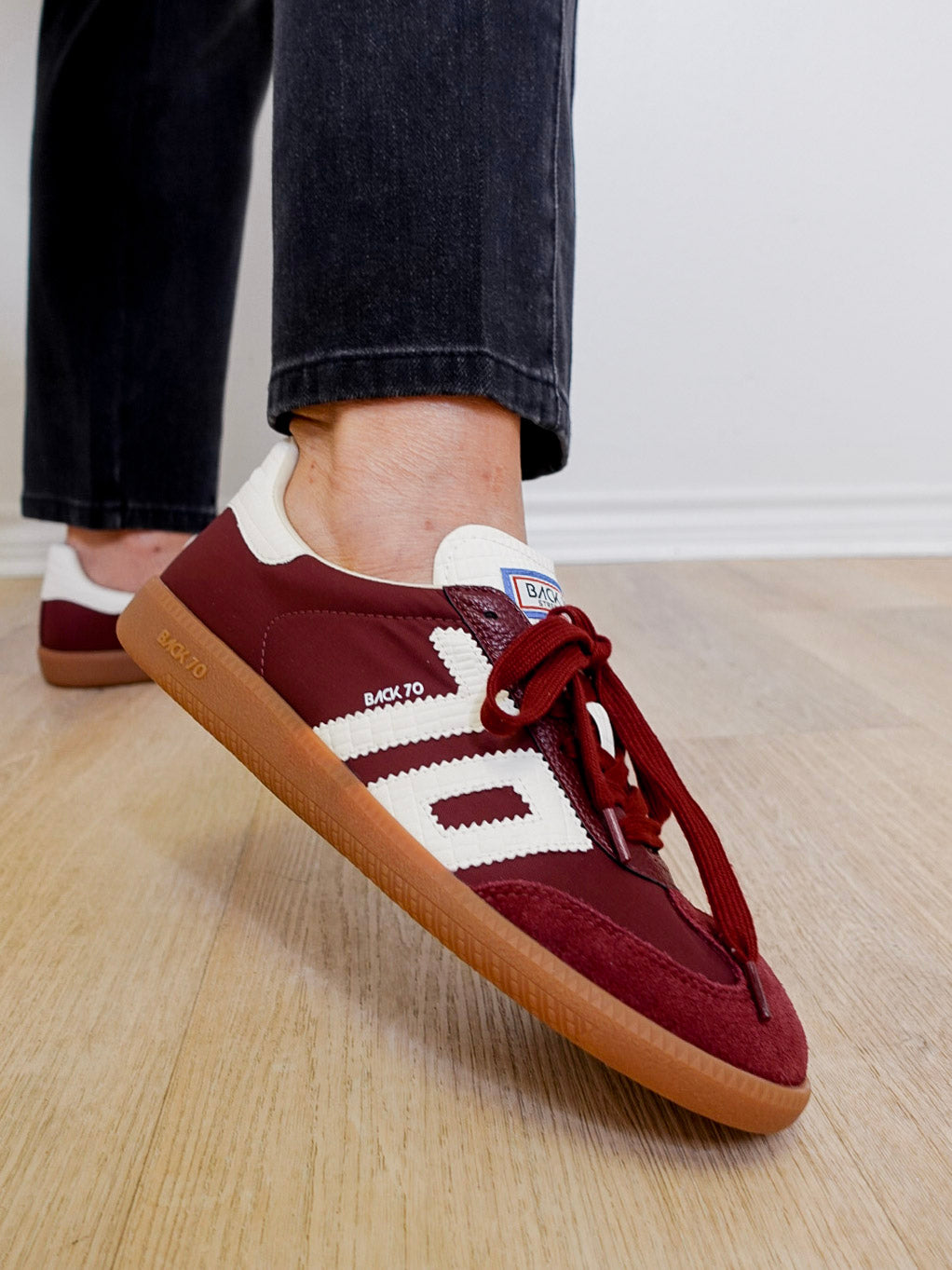 Maroon sneakers with white accents worn indoors on a wooden floor.