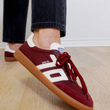 Maroon sneakers with white accents worn indoors on a wooden floor.